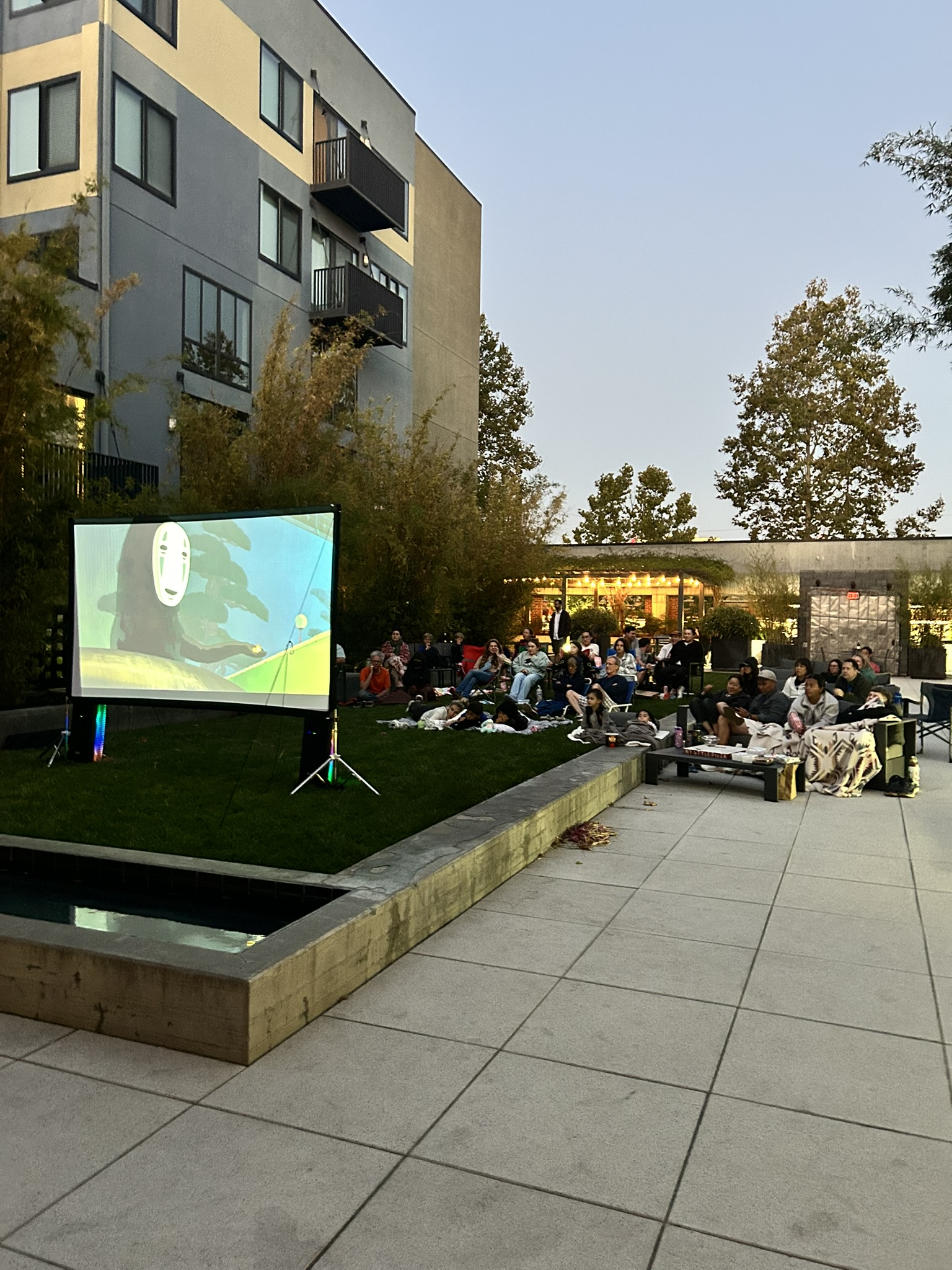 Neighbors gathered on the courtyard green with blankets and chairs for an outdoor movie night